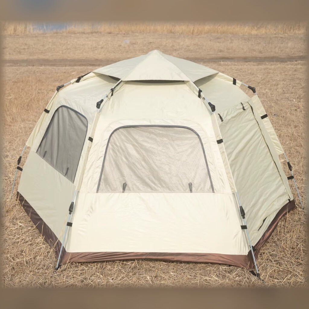 Front view of a beige portable hexagonal camping tent set up outdoors.