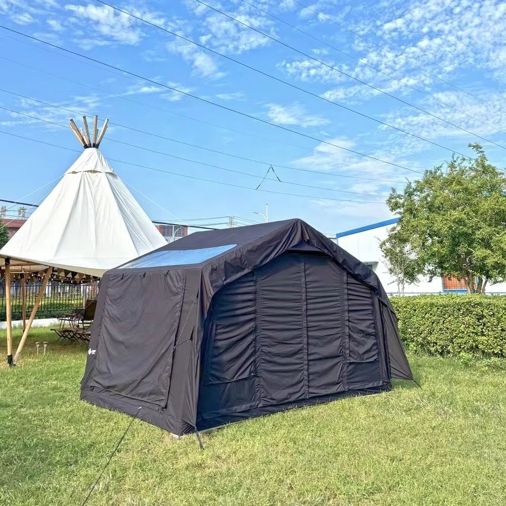 Rear view of a black cabin-style inflatable tent on a grassy campsite.