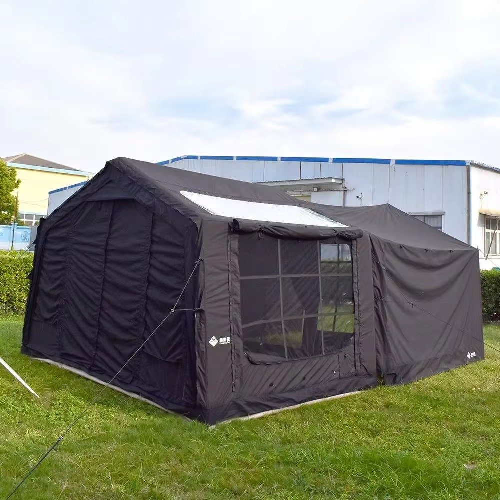 Black inflatable tent with an extended side awning and guy lines on a grassy campsite.
