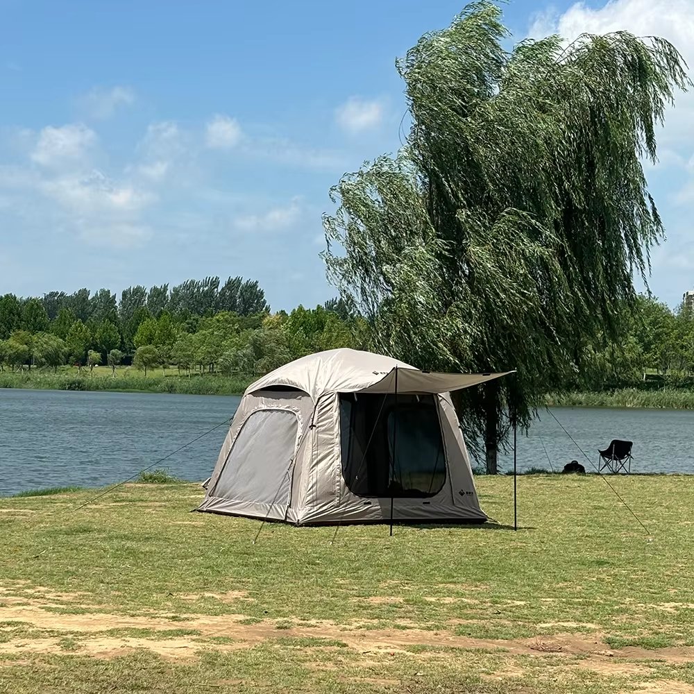 Beige camping tent beside a lake with a willow tree and camping chair nearby