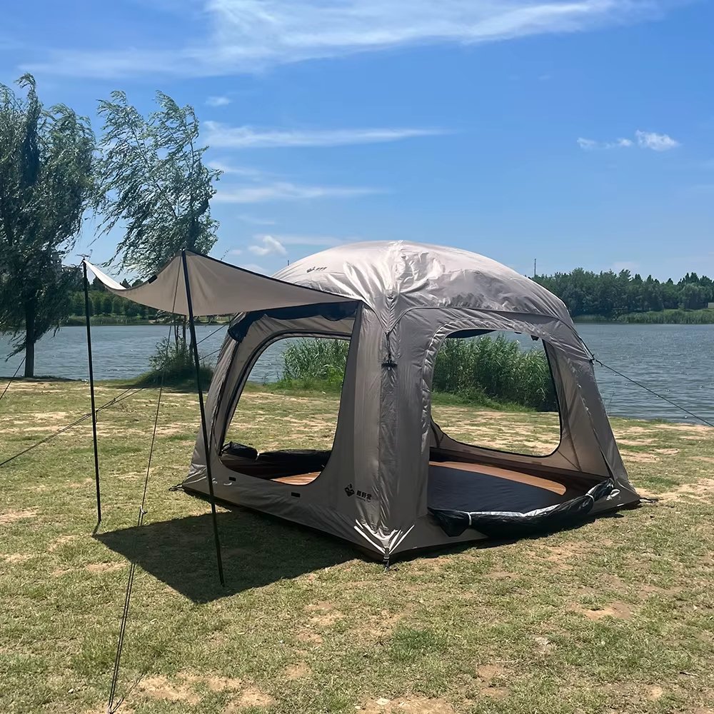 Beige camping tent with an extended awning and mesh doorway beside a lake