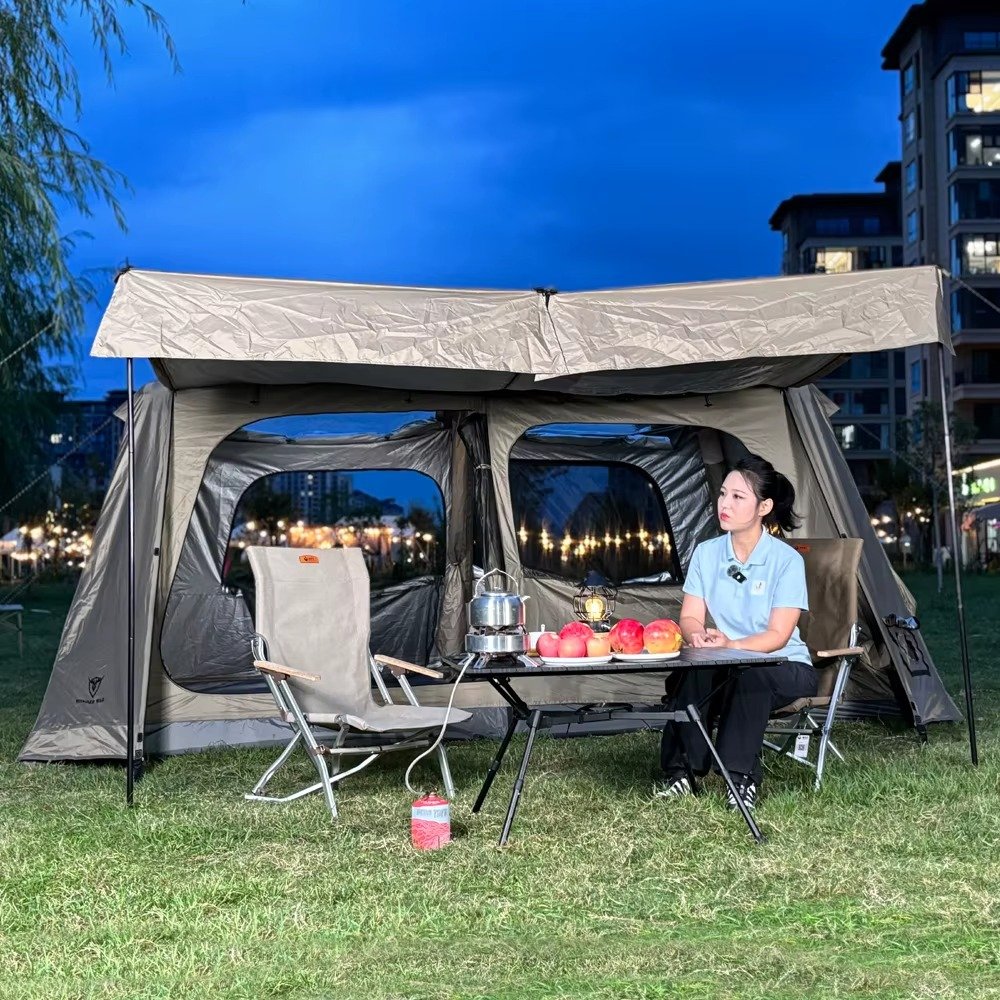 Large light-colored cabin tent with an extended awning and open front at dusk, with a camper seated underneath.
