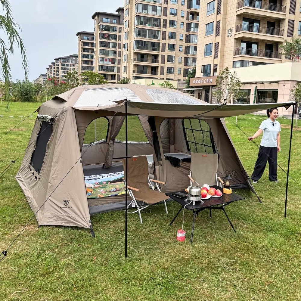 Open cabin tent with roof skylights, extended awning, camping chairs, and a table on grass.