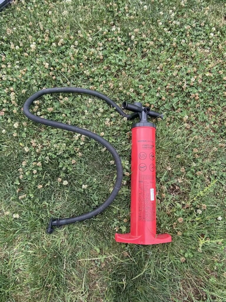 Red manual air pump with a flexible hose displayed on grass.